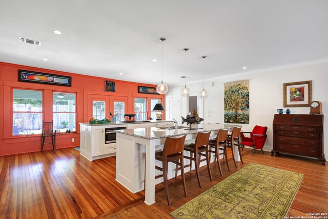 kitchen featuring a kitchen island with sink, white cabinetry, a kitchen breakfast bar, wood-type flooring, and hanging light fixtures