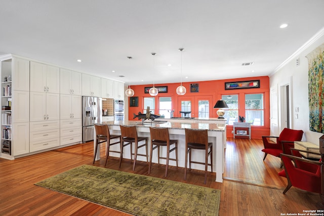 kitchen featuring dark hardwood / wood-style floors, a center island with sink, pendant lighting, stainless steel appliances, and white cabinets