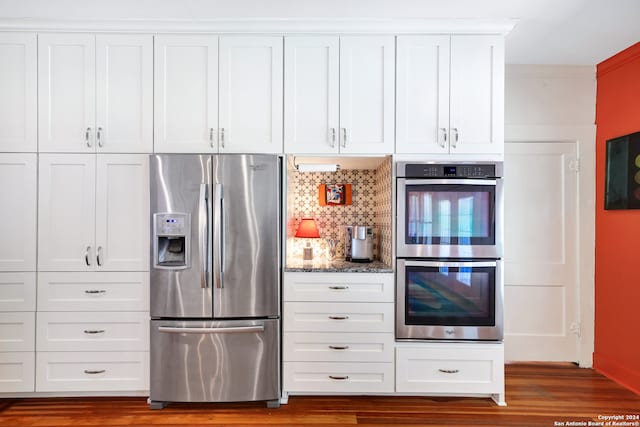 kitchen featuring dark stone counters, white cabinetry, backsplash, appliances with stainless steel finishes, and hardwood / wood-style flooring