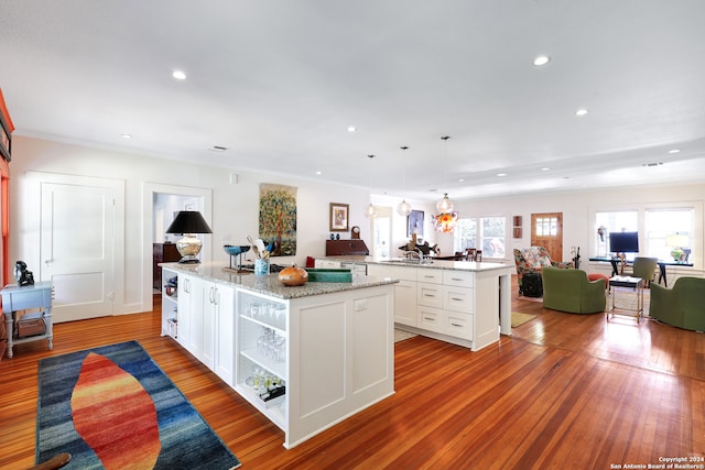 kitchen with decorative light fixtures, a kitchen island, light wood-type flooring, and white cabinetry