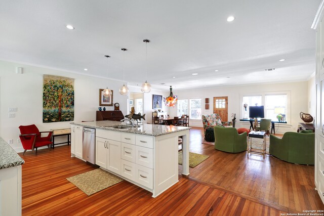 kitchen featuring decorative light fixtures, hardwood / wood-style floors, a kitchen island with sink, stainless steel dishwasher, and white cabinetry