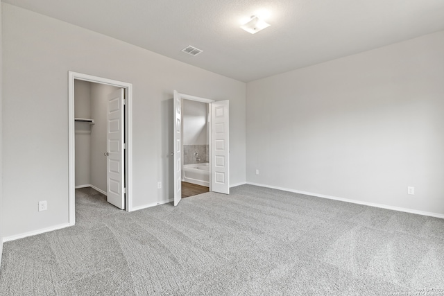 unfurnished bedroom with connected bathroom, a walk in closet, a closet, and carpet floors