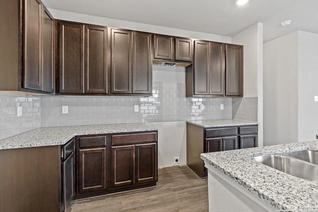 kitchen with dark wood-type flooring, dark brown cabinetry, and light stone countertops