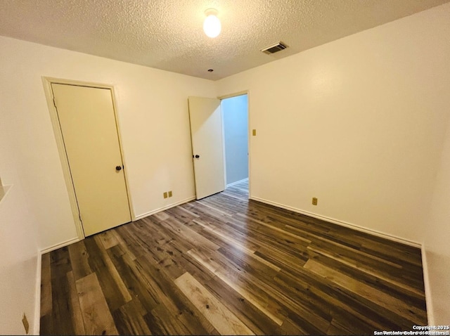 unfurnished bedroom featuring visible vents, a textured ceiling, and dark wood-style flooring