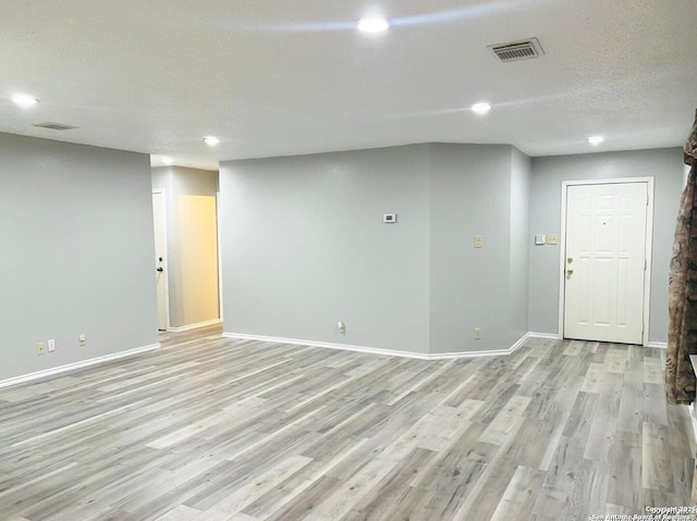 interior space featuring a textured ceiling, baseboards, visible vents, and light wood-type flooring