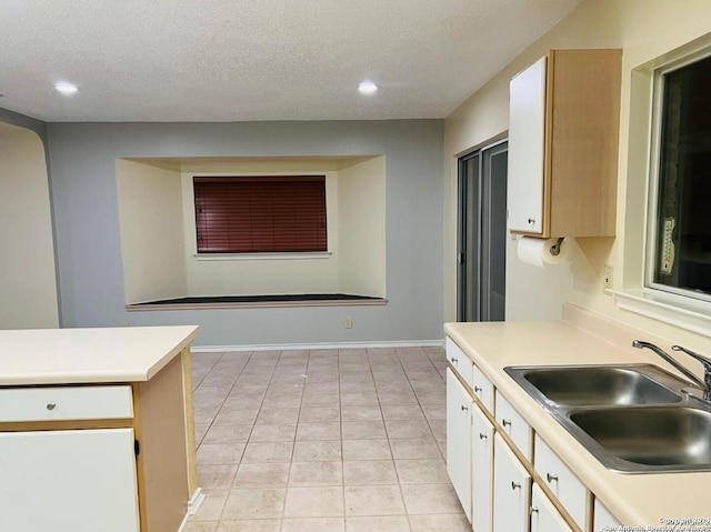 kitchen with light countertops, white cabinets, recessed lighting, and a sink