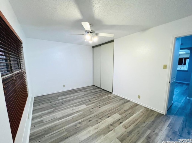 unfurnished bedroom with a textured ceiling, wood finished floors, a closet, baseboards, and ceiling fan