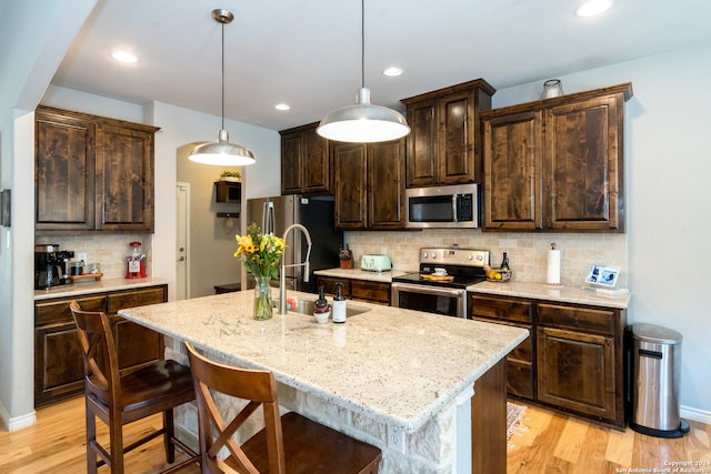 kitchen featuring decorative light fixtures, dark brown cabinets, a center island with sink, appliances with stainless steel finishes, and light wood-type flooring