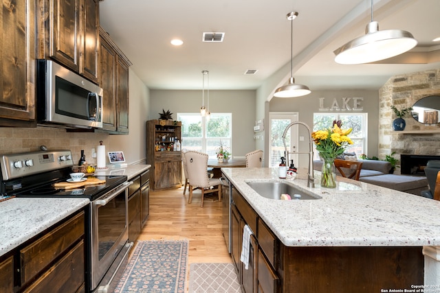 kitchen featuring a fireplace, stainless steel appliances, light hardwood / wood-style floors, sink, and a kitchen island with sink