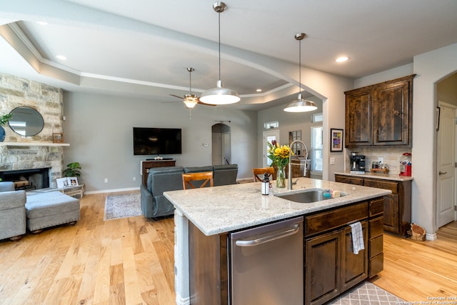 kitchen with light hardwood / wood-style floors, sink, a tray ceiling, a stone fireplace, and a kitchen island with sink