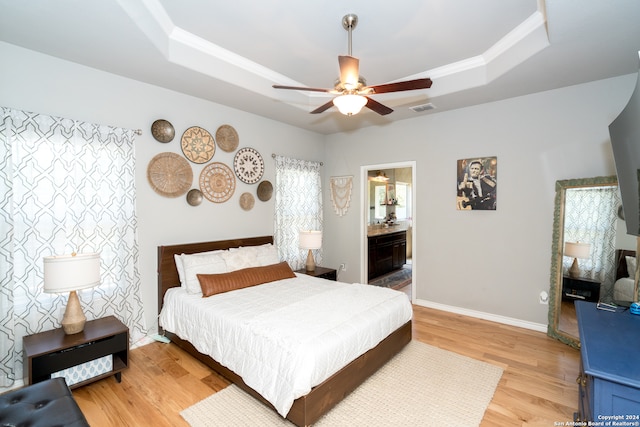 bedroom featuring ceiling fan, ensuite bathroom, a tray ceiling, and light hardwood / wood-style floors