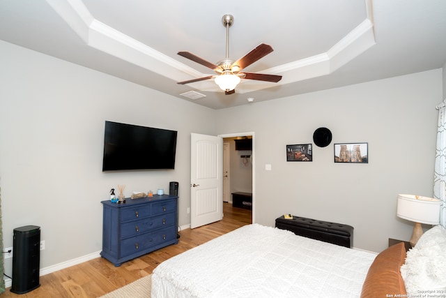 bedroom with light wood-type flooring, a tray ceiling, ceiling fan, and ornamental molding