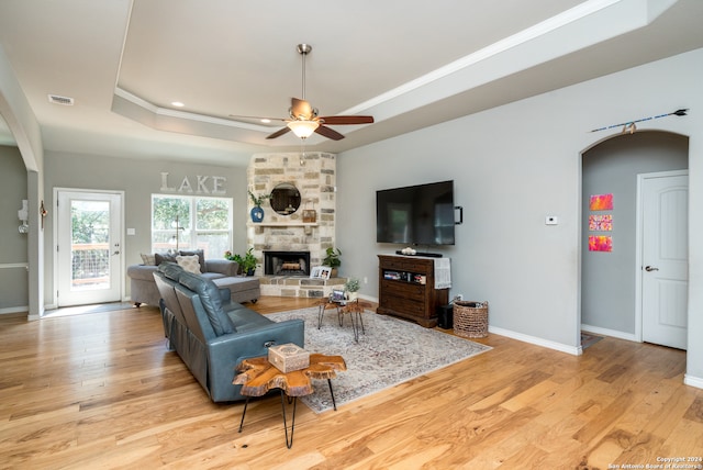 living room with light hardwood / wood-style floors, ceiling fan, a raised ceiling, and a stone fireplace