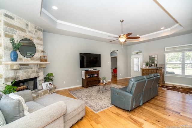 living room featuring a raised ceiling, wood-type flooring, ceiling fan, and a stone fireplace