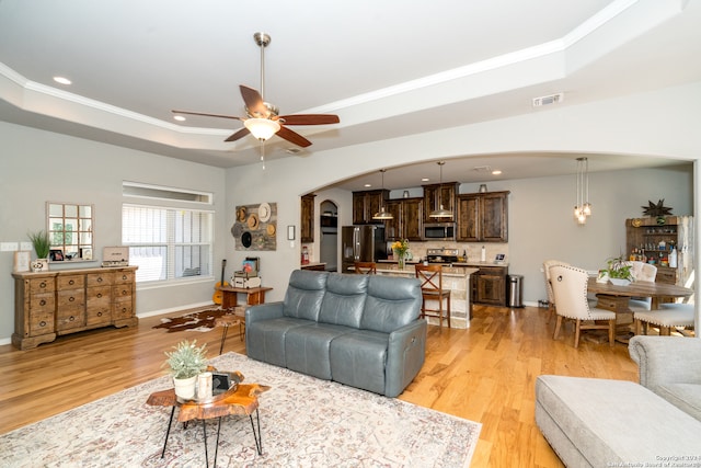 living room featuring light wood-type flooring, crown molding, a tray ceiling, and ceiling fan