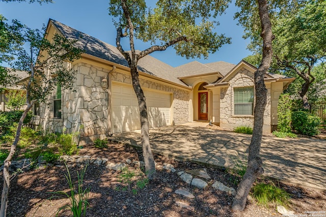 view of front facade with stone siding, driveway, roof with shingles, and an attached garage