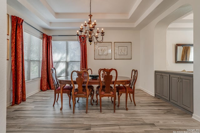 dining area featuring baseboards, a tray ceiling, light wood-style flooring, and a chandelier
