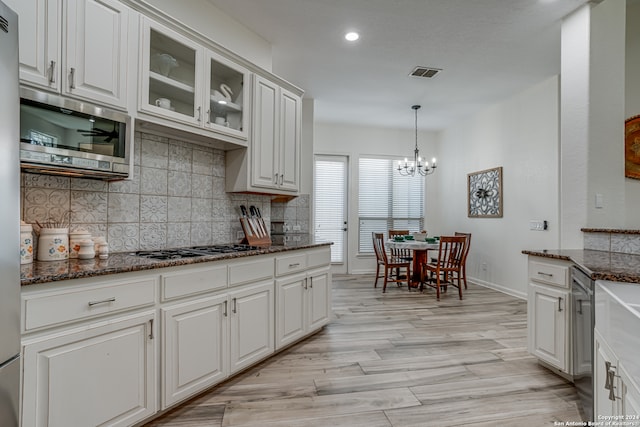 kitchen featuring dark stone counters, white cabinetry, stainless steel appliances, an inviting chandelier, and light hardwood / wood-style floors