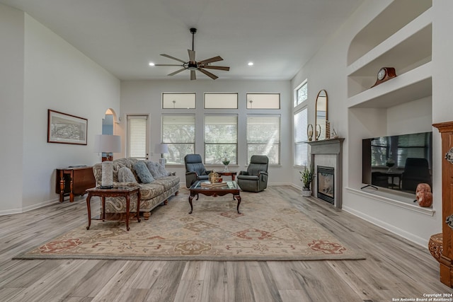 living area featuring baseboards, wood finished floors, a glass covered fireplace, and a ceiling fan