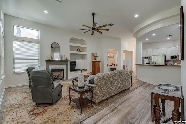 living room with a fireplace, light wood-type flooring, built in features, visible vents, and arched walkways