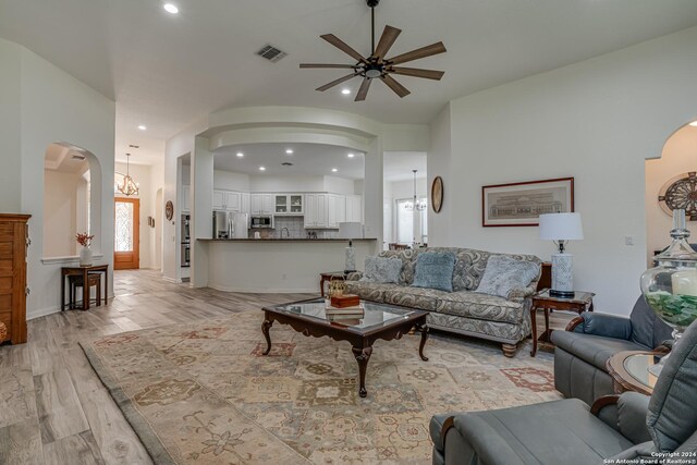living area featuring light wood-style flooring, ceiling fan with notable chandelier, visible vents, arched walkways, and recessed lighting
