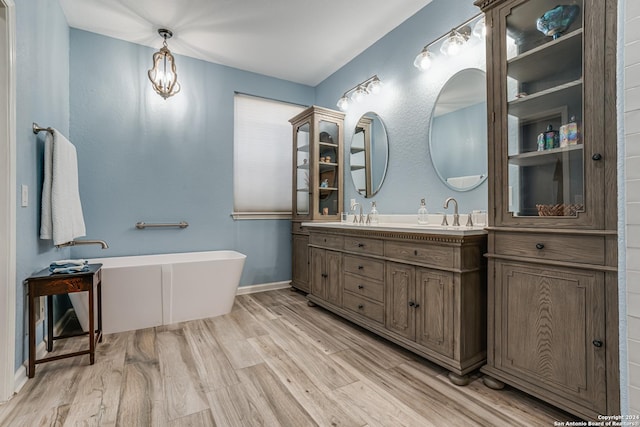 bathroom with double vanity, a freestanding bath, wood finished floors, and a sink