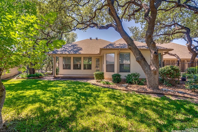 rear view of house featuring stucco siding, fence, roof with shingles, and a yard