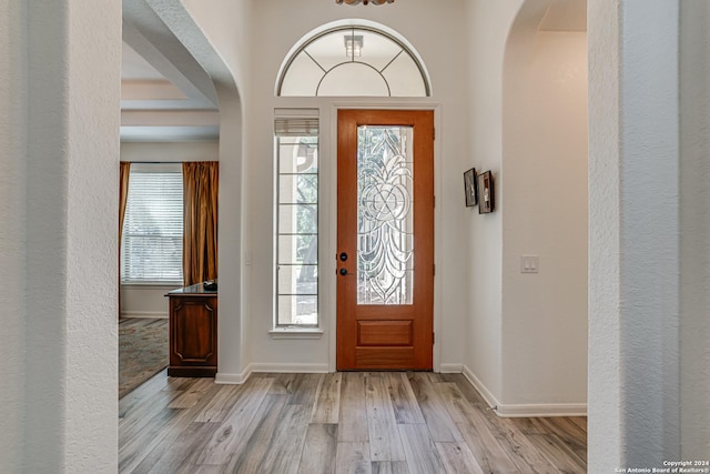 entryway with arched walkways, baseboards, and light wood-type flooring