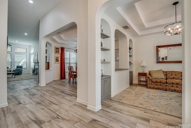 hallway featuring light wood-style flooring, plenty of natural light, a notable chandelier, and a tray ceiling