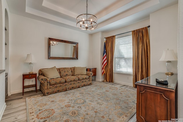 living area with a raised ceiling, baseboards, a chandelier, and light wood-type flooring