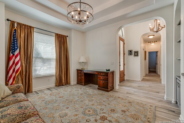 office area featuring a tray ceiling, light wood-type flooring, a chandelier, arched walkways, and visible vents