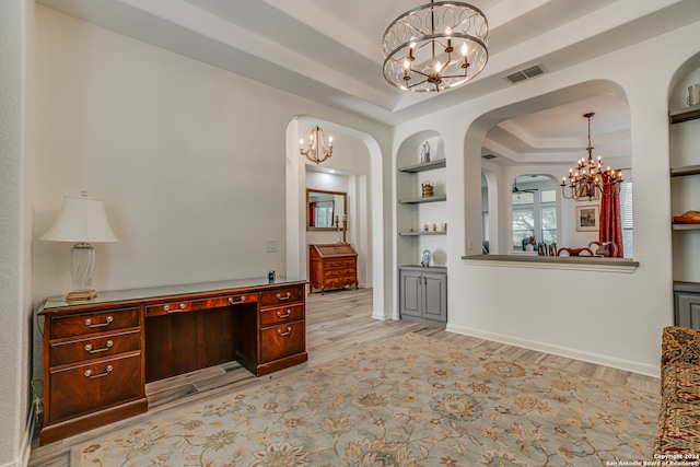 office space with built in features, an inviting chandelier, a tray ceiling, and light hardwood / wood-style floors