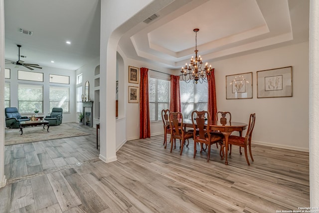 dining room with a raised ceiling, ceiling fan with notable chandelier, light wood-style floors, and a wealth of natural light