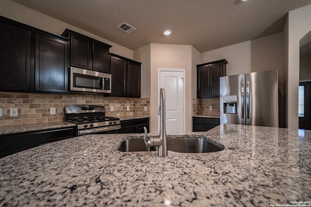 kitchen with visible vents, a sink, backsplash, appliances with stainless steel finishes, and light stone countertops