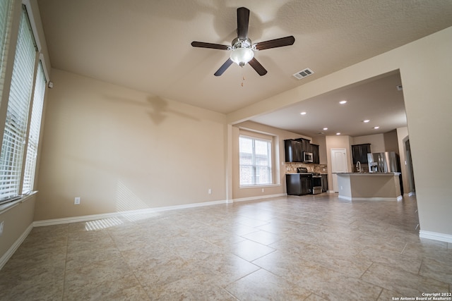 unfurnished living room featuring ceiling fan, sink, light tile patterned flooring, and a textured ceiling