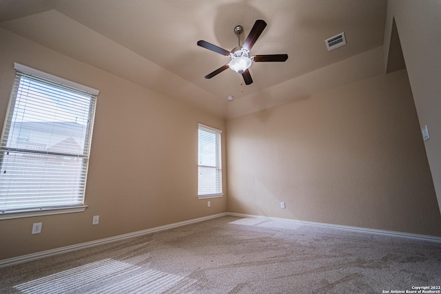 carpeted empty room with vaulted ceiling, a ceiling fan, visible vents, and baseboards