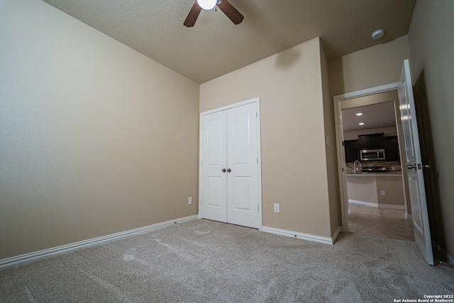 unfurnished bedroom featuring light carpet, vaulted ceiling, a textured ceiling, and ceiling fan