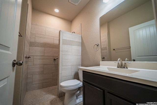 bathroom featuring vanity, visible vents, a tile shower, toilet, and a textured wall