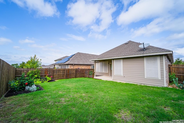 rear view of house with a fenced backyard, a yard, and roof with shingles