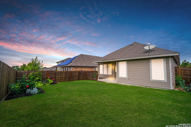 back of property at dusk featuring a yard, a fenced backyard, and a shingled roof