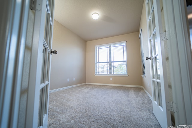 carpeted empty room featuring vaulted ceiling, a textured ceiling, and french doors