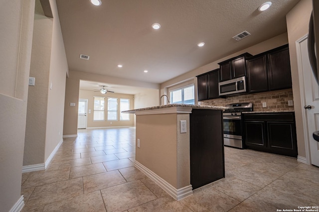 kitchen with stainless steel appliances, visible vents, an island with sink, and decorative backsplash