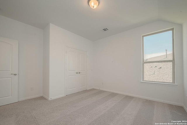 unfurnished bedroom with light colored carpet, lofted ceiling, and a closet