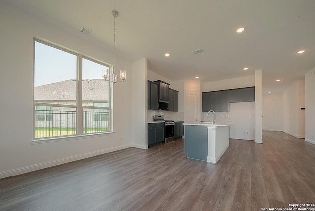 kitchen featuring decorative backsplash, hardwood / wood-style flooring, an inviting chandelier, a center island with sink, and stainless steel stove