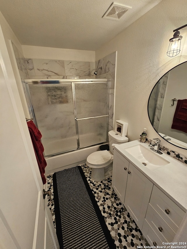 full bathroom featuring toilet, bath / shower combo with glass door, a textured ceiling, and vanity