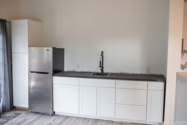 kitchen featuring white cabinets, light hardwood / wood-style flooring, stainless steel refrigerator, and sink