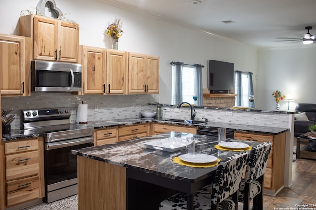 kitchen with appliances with stainless steel finishes, a kitchen island, decorative backsplash, and ceiling fan