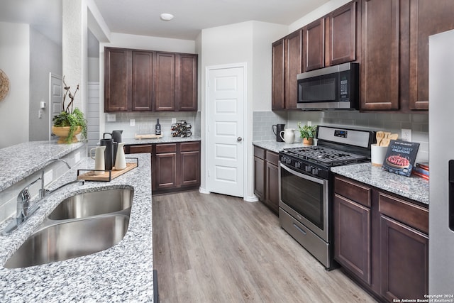 kitchen featuring light hardwood / wood-style floors, tasteful backsplash, sink, stainless steel appliances, and light stone countertops