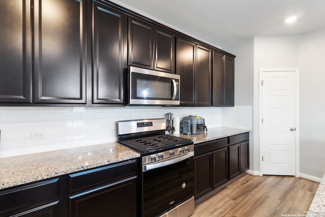 kitchen with backsplash, light wood-type flooring, light stone countertops, stainless steel appliances, and dark brown cabinets