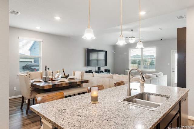 kitchen with a kitchen island with sink, dark hardwood / wood-style flooring, light stone counters, sink, and hanging light fixtures